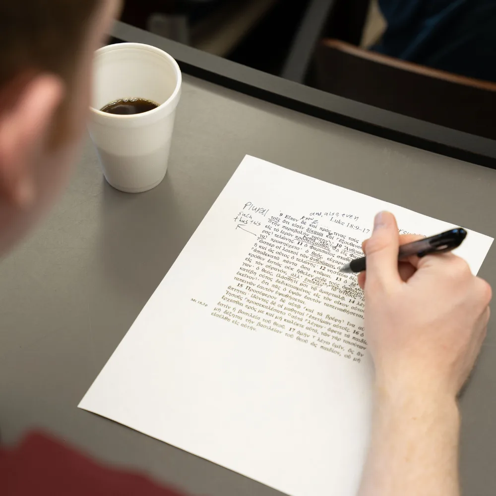 Two students read handouts during a session, with fall colors outside the window.